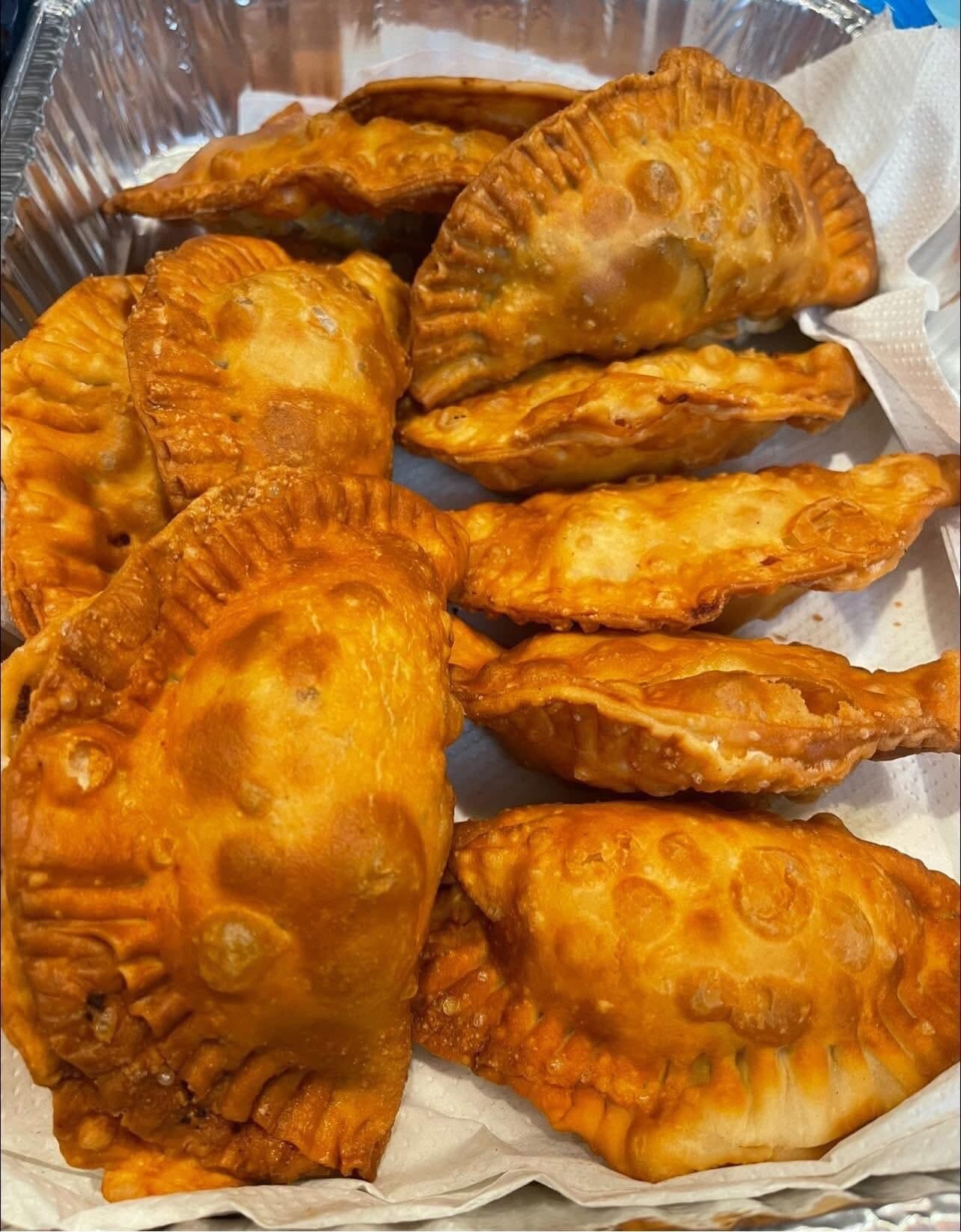 A foil tray lined with paper towel, piled with golden fried KDM empanadas